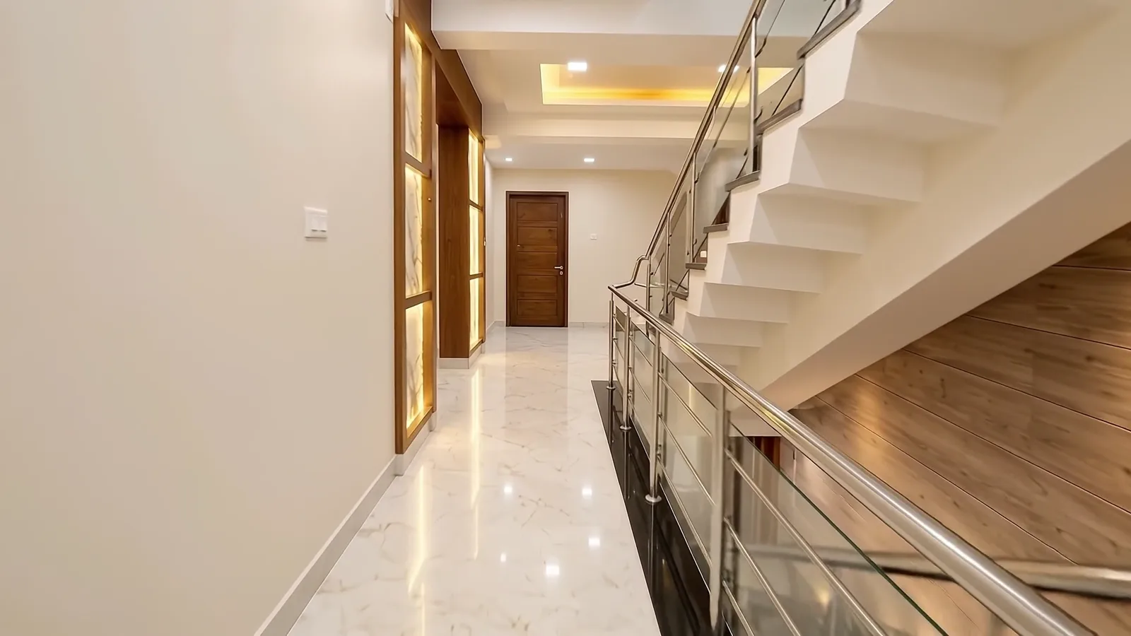 Marble corridor with a glass-railed staircase and warm cove lighting